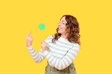 Happy woman with paper clover on yellow background. St. Patrick's Day