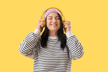 Beautiful happy mature woman in headphones on yellow background. International Women's Day