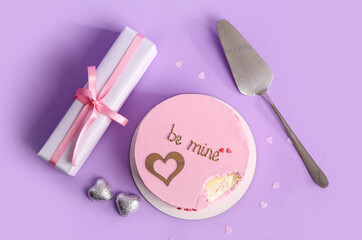 Bitten bento cake with gift box and spatula on purple background. Valentine's Day celebration