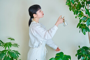 部屋の置いた観葉植物に水やりをする若い女性