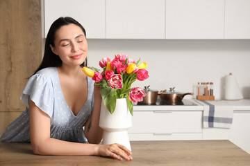 Young woman and vase with bouquet of beautiful tulips in kitchen. International Women's Day