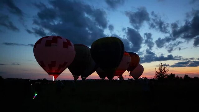 Eight air balloons prepared to fly on field with people during sunset
