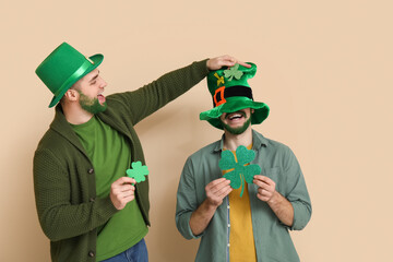 Young men in leprechaun hats with green beards holding clover on beige background. St. Patrick's...