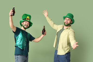 Happy young men in leprechaun hats with green beards holding bottles of beer on green background....