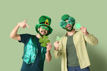 Young men in leprechaun hats and decorative glasses with green beards holding clover on green...