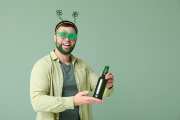 Young man in headband and decorative glasses in shape of clover with green beard holding bottle of...