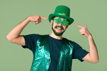 Young man in leprechaun hat with green beard pointing at decorative glasses in shape of clover on...