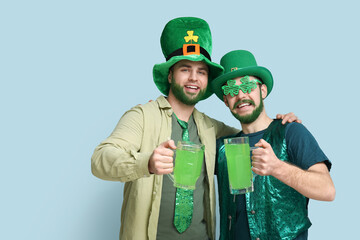 Young men in leprechaun hats with green beards holding glasses of beer on blue background. St....