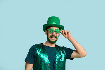 Young man in leprechaun hat and decorative glasses in shape of clover with green beard on blue...