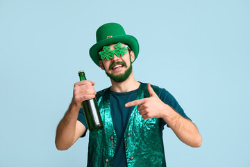 Young man in leprechaun hat and decorative glasses in shape of clover with green beard pointing at...