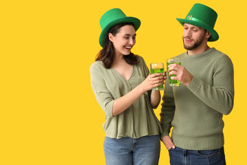 Beautiful young couple in leprechaun hats with glasses of beer on yellow background. St. Patrick's...