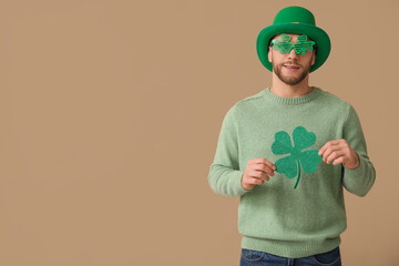 Young man in leprechaun hat and decorative glasses with clover on brown background. St. Patrick's...