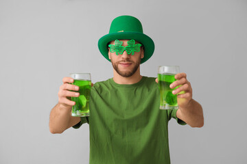 Young man in leprechaun hat with glasses of beer on grey background. St. Patrick's Day celebration