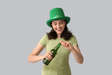 Beautiful young woman in leprechaun hat with bottle of beer on grey background. St. Patrick's Day...