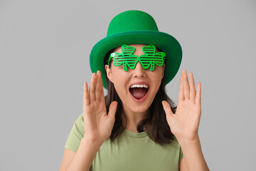 Beautiful young woman in leprechaun hat and decorative glasses in shape of clover on grey...