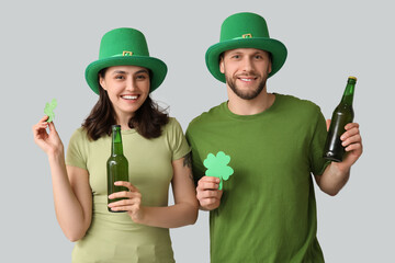 Happy young couple in leprechaun hats with bottles of beer and clover on grey background. St....