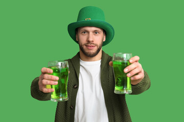 Young man in leprechaun hat with glasses of beer on green background. St. Patrick's Day celebration