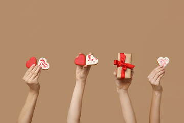 Women with heart-shaped cookies and gift box on brown background. Valentine's Day celebration