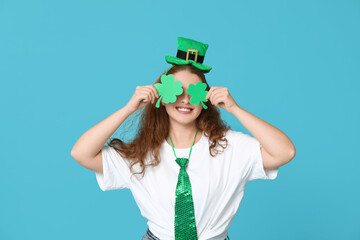 Young redhead woman with paper clovers on blue background. St. Patrick's Day celebration