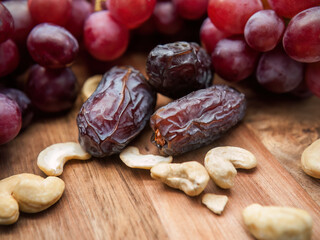 Royal large dates close up on a wooden background with cashew nuts and grapes in the background. Selective focus. Horizontal.