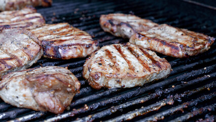 Grilled meat steak on stainless BBQ grill with flames on dark background. Food and cuisine concept.