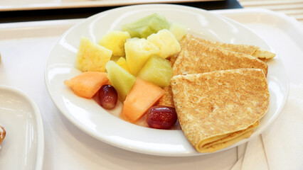 Delicious fresh fruits and freshly baked pancakes on white plate. Breakfast at restaurant.