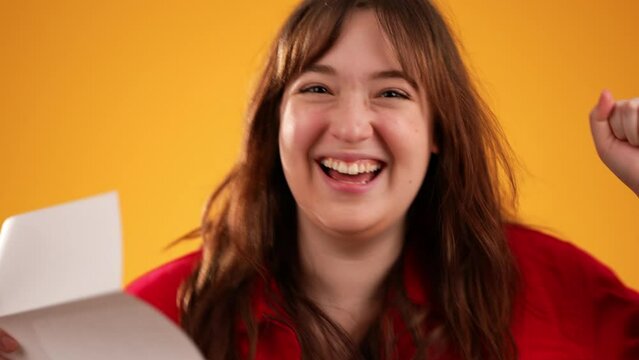 Closeup portrait of woman opening letter with good news looks at camera a smiling and happy isolated on yellow background.