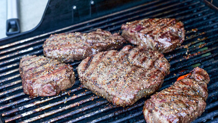 Grilled meat steak on stainless BBQ grill with flames on dark background. Food and cuisine concept.
