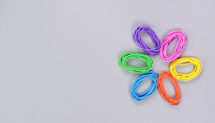 Multicolored flower made of elastic. Top view of colorful rubber bands isolated on grey. Rainbow elastic rubber bands on white. Rainbow flower shape.