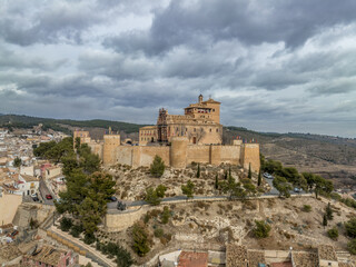 Fototapeta na wymiar Aerial view of Caravaca de la Cruz castle dominating the landscape with square and circular towers, medieval palace and Baroque ornament facade church