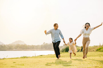 Happy family on vacation, running and laughing together in a green field, with the sun setting in...