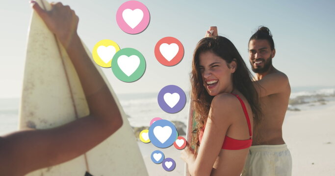 Image of heart digital icons over friends with surfboards on beach
