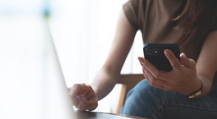 Casual business woman typing on laptop computer and using mobile phone, online working, surfing the internet at home office, close up, freelance at work, telecommuting, business and technology