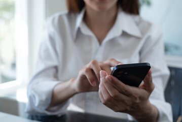 Close up of businesswoman using mobile smart phone during working on laptop computer at office. Asian business woman hand holding smartphone, connecting the internet