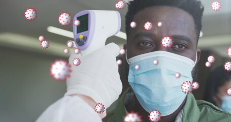 Image of covid-19 cells floating with man having temperature checked wearing face masks