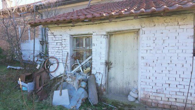 Whitewashed brick shed with a red slate roof and a wooden door with some junk piled up in front of it. Shot in the village of Bogdan, Bulgaria