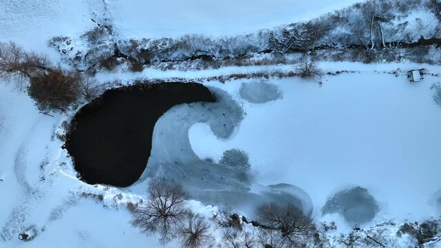 Top down aerial of farm pond partially frozen and covered in winter snow and ice. Rising reveal shot.