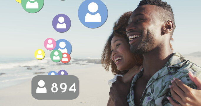 Profile icons with increasing numbers floating against african american couple smiling on the beach - Powered by Adobe