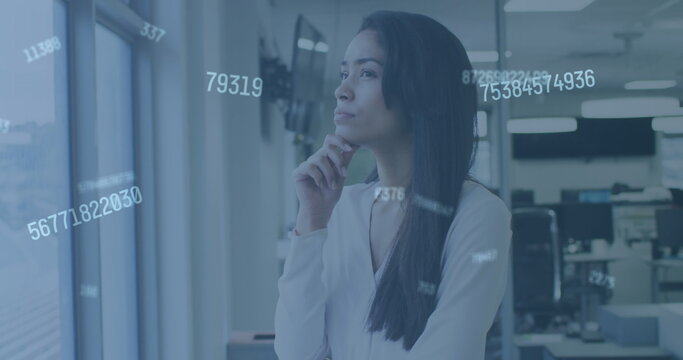 Image of digital interface showing floating numbers and a woman looking through window in an office - Powered by Adobe