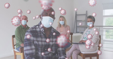 Multiple covid-19 cells floating against group of people wearing face mask sitting at home