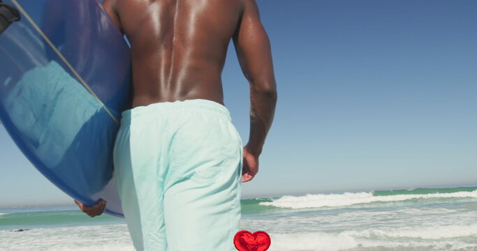 Image of heart digital icons over man carrying surfboard on beach
