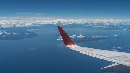 Obraz premium The islands of Malaysia are visible from the window of the plane. White clouds, blue sky, calm ocean. The wing of the aircraft is in the foreground.