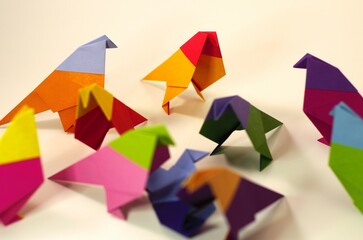 Overhead view of several origami birds in the middle of attacking a blue origami bird. In the...