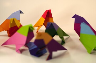 Overhead view of several origami birds in the middle of attacking a blue origami bird. In the background an orange and red bird stands apart, and several of the attack birds are turned as if noticing.