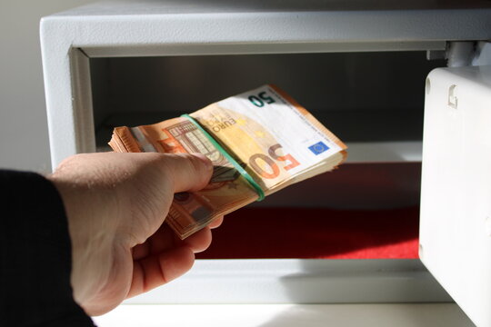 A man holds a stack of fifty euro notes in his hand and puts it in the safe deposit box. The concept of safe storage of funds.
