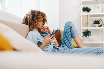 Happy Woman Holding Phone and Relaxing on Sofa at Home