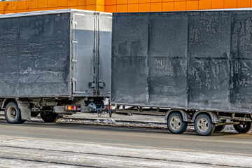 A truck with a trailer is parked at the curb on a winter day