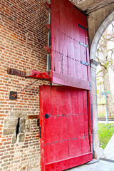 Old red wooden door divided into two parts at one of the entrances to Alden Biesen castle against a brick wall, known as Dutch or stable door, Bilzen, Limburg, Belgium