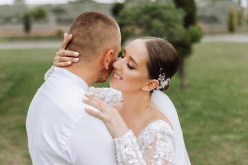 Fototapeta premium The bride and groom embrace. The bride gently hugs the groom by the shoulders. Beautiful wedding couple. The concept of romance in a newlyweds relationship. Honeymoon.
