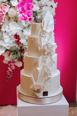 a four-tiered white wedding cake stands on a decorative stand. Decorative wedding cake. Beauty is in the details.